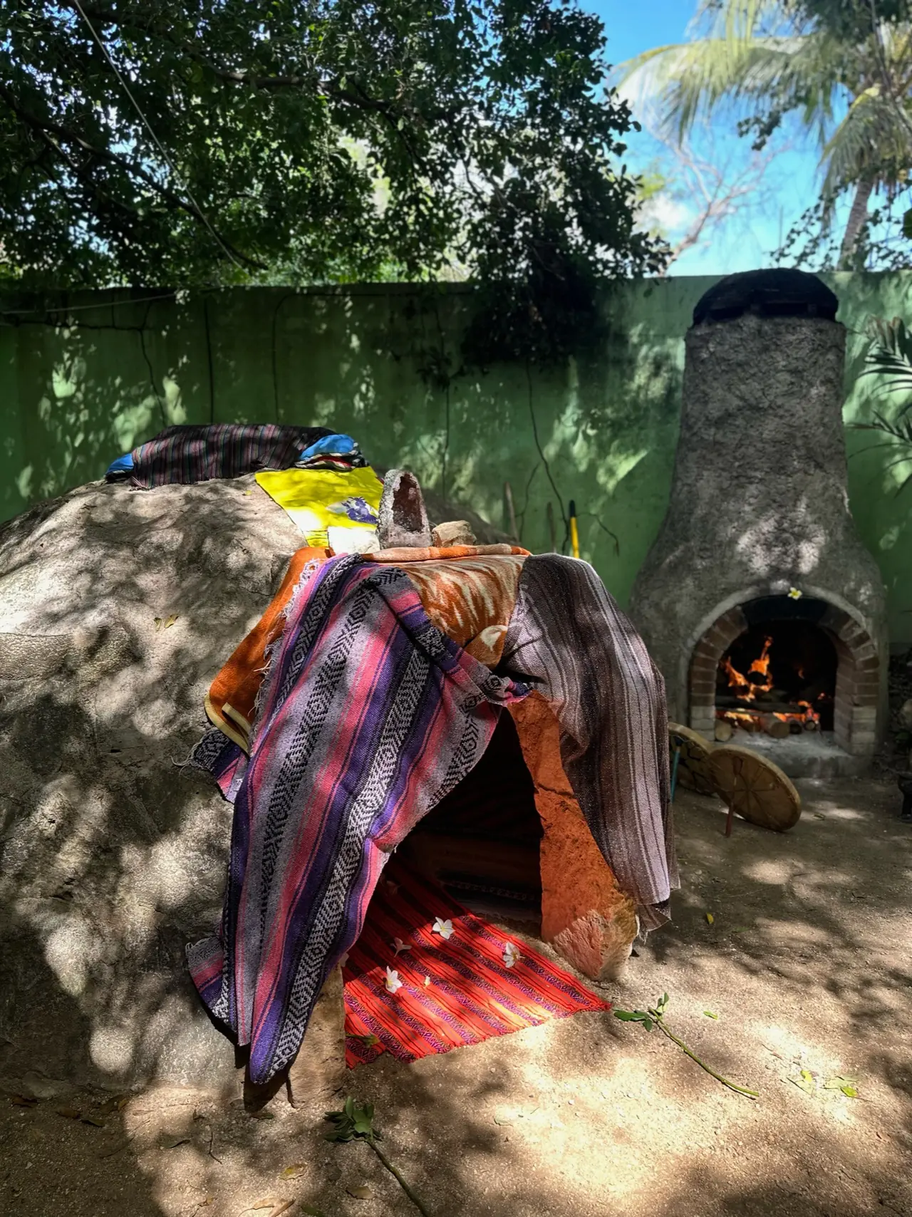Temazcal de patio cubierto con sarapes, junto al horno de piedra encendido