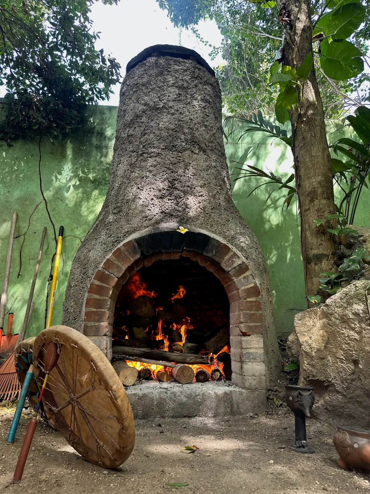 A lit stone oven in the yard, with a drum leaning beside it
