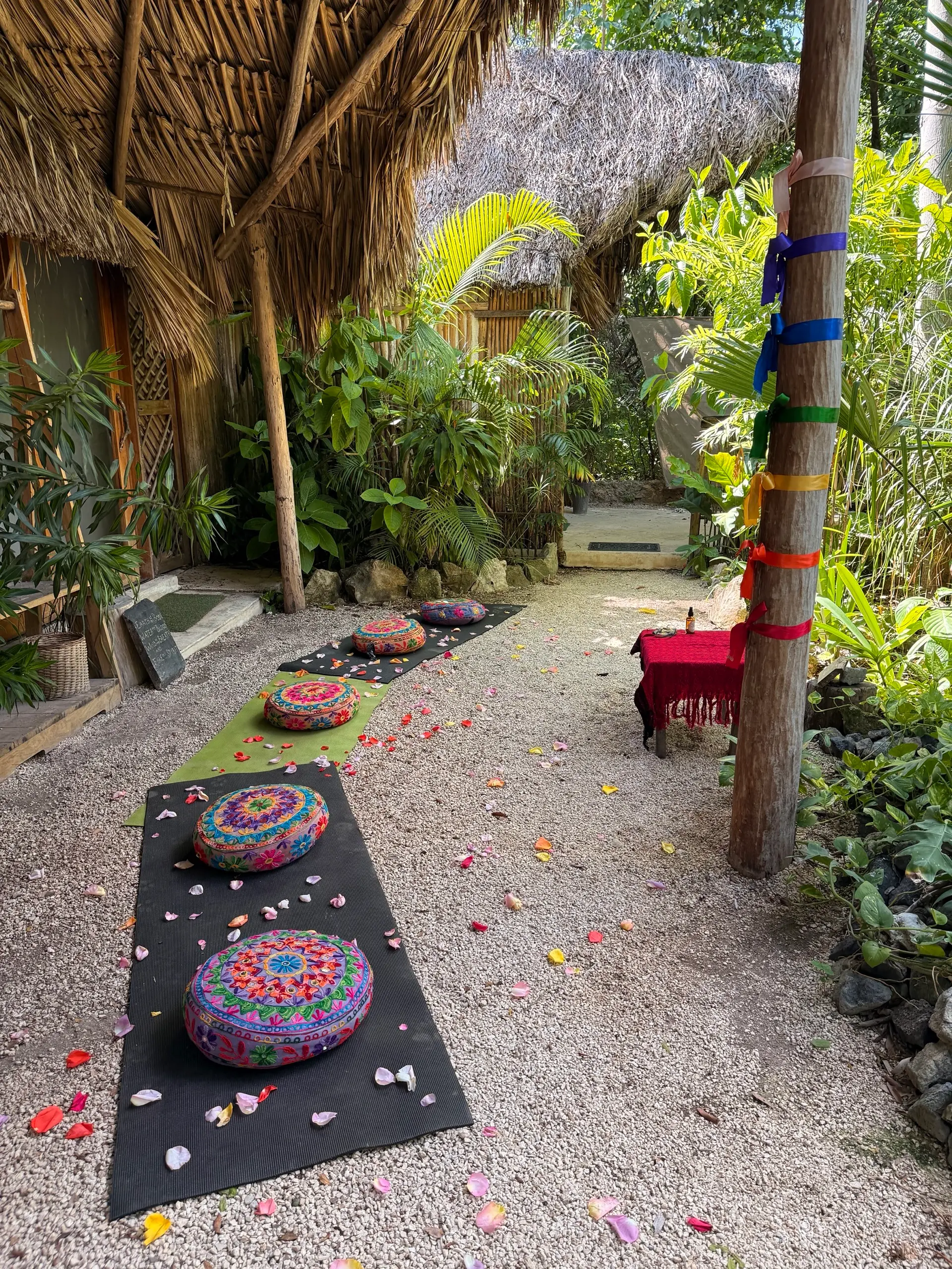 The post with the seven-chakra ribbons, the embroidered cushions and petals on the ground