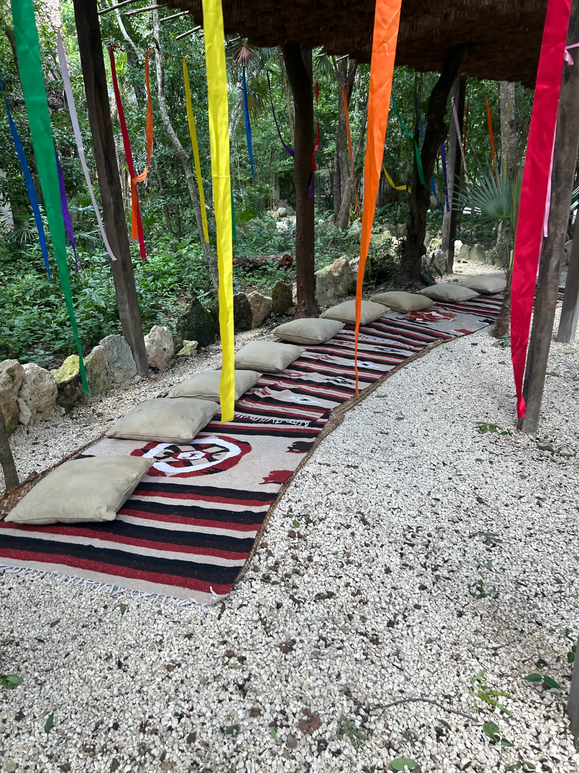 Sendero de tapetes y listones de colores que conduce al temazcal, entre la selva